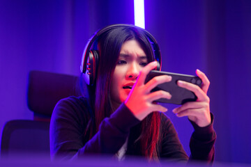 Stressed Boring Young pretty asian woman in headphone playing game. Chinese female Gamer holding cell phone play video game online feeling sadness. Loss and Missed the chance to become a champion