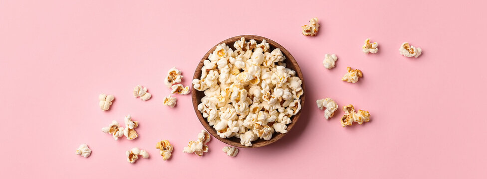 Bowl of tasty popcorn on pink background, top view