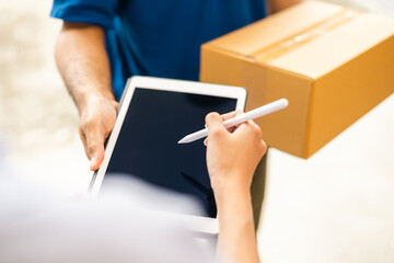 Hand woman signing electronic Signature on tablet for agreement of contract digital receiving parcel from blue delivery man from shopping online. Courier man delivering package to destination.
