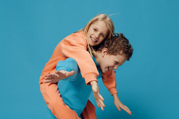 two cute, joyful children in multi-colored sweaters stand on a blue background, a boy rolls a happy girl on his back. The theme of children's friendship and relationships
