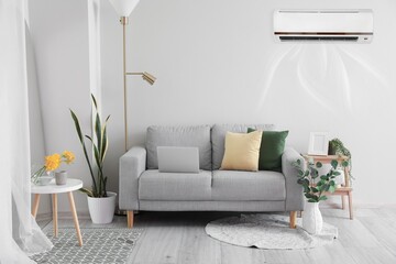 Stylish sofa and in light room with operating air conditioner