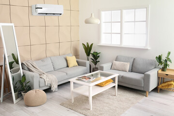 Interior of stylish living room with comfortable sofas, mirror, table and air conditioner