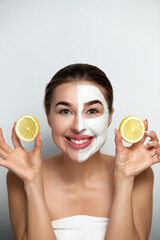 Beautiful of smiling young woman with a white mask of clay on face ..Girl model beauty face holding slices of fresh lemon. Cosmetic mask . Skin care . Spa treatment. Cosmetology
