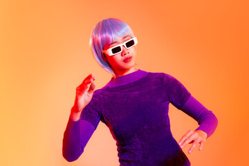 Young asian woman acting robot in purple dress wearing white sunglasses posing on the orange background. Future cyborg girl and metaverse concept.