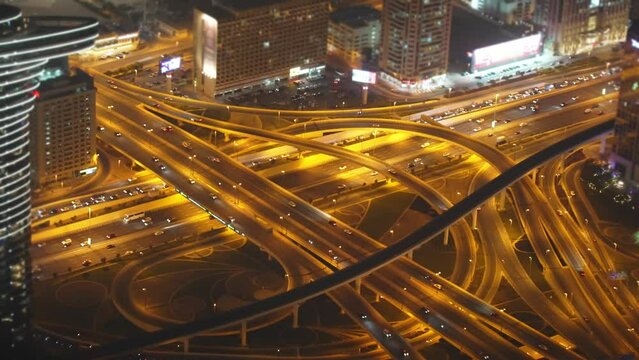 Multi-level illuminated road Burj Khalifa from bird eye view at night in Dubai in UAE. Intersection of fork of expressway highways. Top view of traffic cars on motorway. Architectural construction.