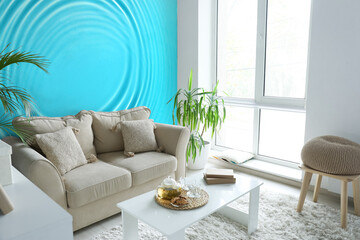 Cozy sofa and table near wall with print of clear blue water