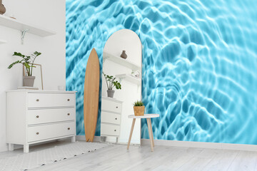 Interior of living room with surfboard, chest of drawers and mirror near wall with print of clear blue water