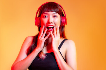 Young asian woman in black tank top wearing red headphones listen to music online on orange color background.
