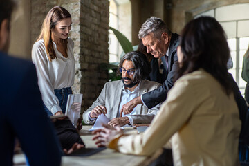 Businessman of middle eastern ethnicity signing a contract sitting on a desk with other businesspersons - business people lifestyle agreement concept
