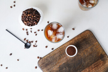 Glass of cold brew with milk and scattered coffee beans on white table