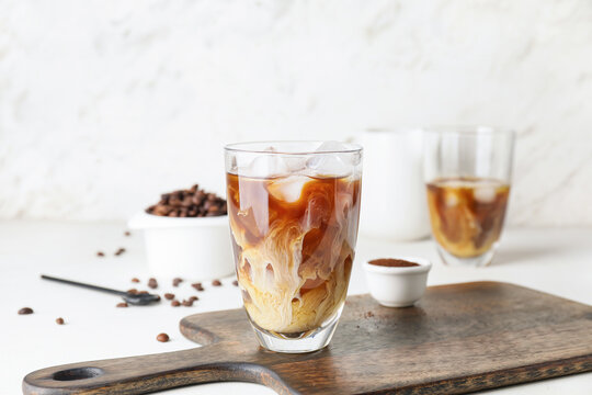 Glass of cold brew coffee with milk on wooden board against light background