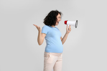 Young pregnant woman shouting into megaphone on light background