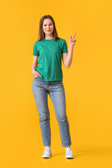 Fototapeta premium Pretty young woman in green t-shirt pointing at something on yellow background