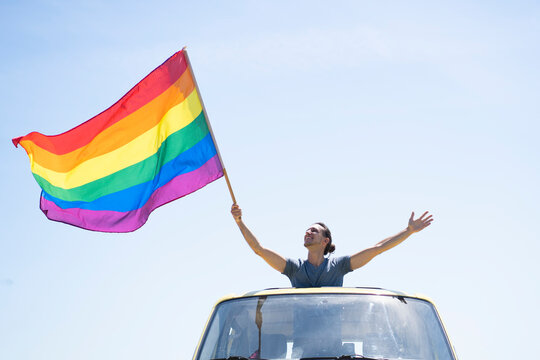 Smiling man with rainbow flag standing in van on sunny day