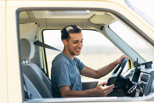 Smiling man surfing net through mobile phone sitting in van