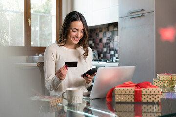 Happy woman with credit card doing online shopping through smart phone at home