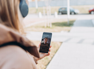 Happy young woman holding smartphone, using mobile phone app for video call on city background. Virtual talking with friends. Girl having a video chat with man on smart phone outdoors