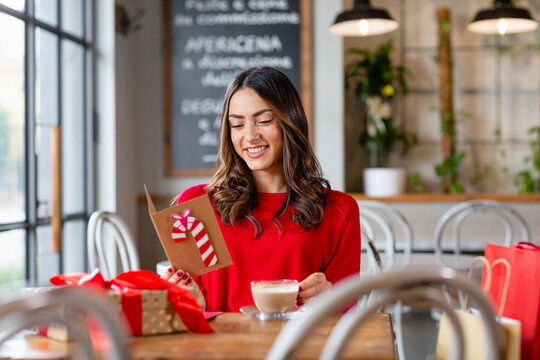 Happy beautiful woman reading Christmas card sitting in cafe