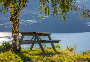 Empty wooden table with chairs on the hill of a summer park at the Okanagan Lake. Sunny warm day by the lake.