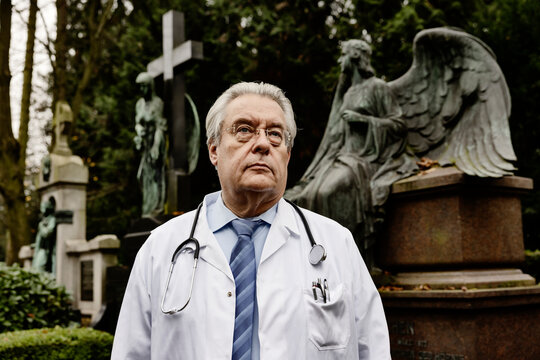 Senior doctor with stethoscope standing on cemetery