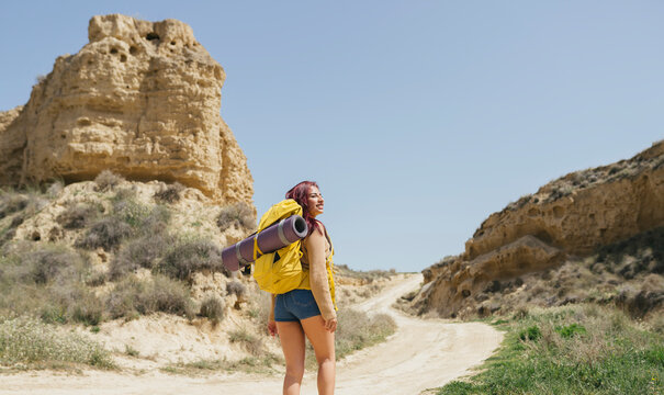 Smiling woman wearing backpack hiking on dirt road