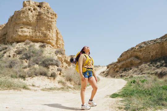 Smiling young woman wearing backpack standing on dirt road