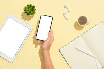 Female hand with mobile phone, tablet computer, earphones, notebook and cup of coffee on color background