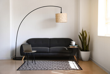 Comfortable sofa, houseplant and lamp near white wall