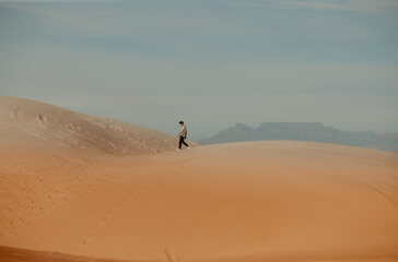 Fototapeta na wymiar Young man walking in hot desert dunes in afternoon sun