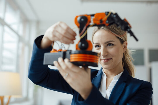Smiling businesswoman analyzing robotic arm model in office
