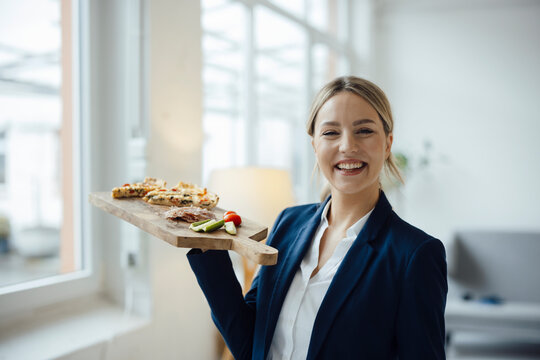 Smiling beautiful businesswoman with sandwich on cutting board in office