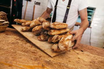 Baker holding tray of fresh baguettes in bakery