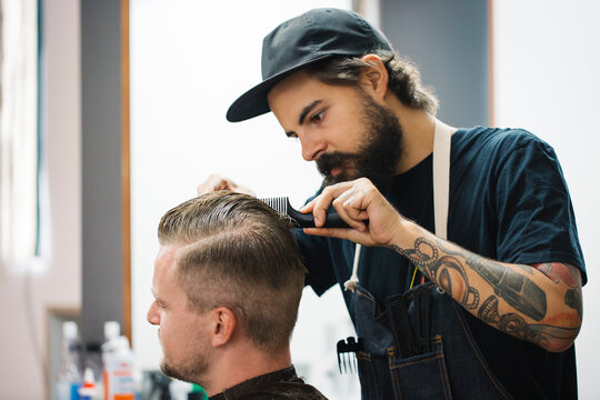 Young hairdresser styling hair of customer at barber shop