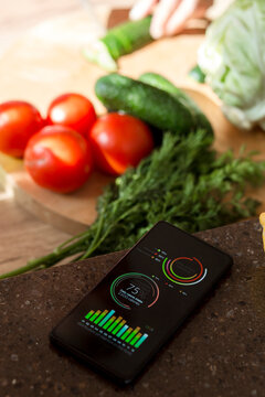 Smartphone with charts on kitchen counter next to vegetables