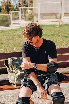 Man sitting on bench adjusting elbow pad at park
