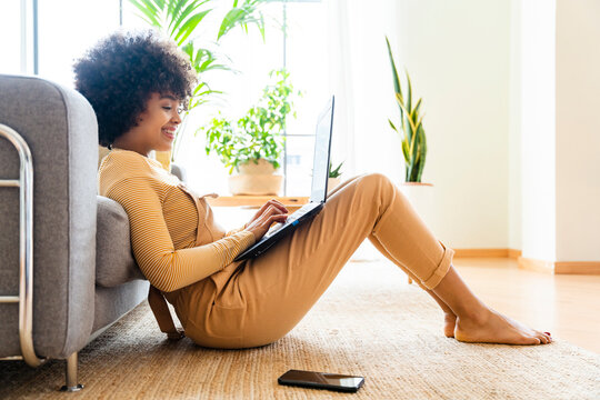 Happy Woman Using Laptop Leaning On Sofa At Home