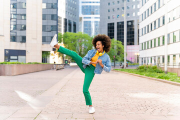 Happy woman with Afro hairstyle kicking on footpath
