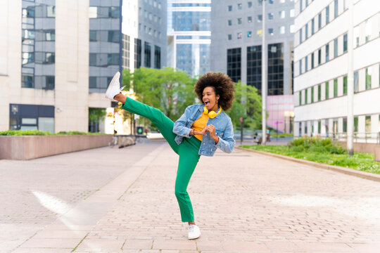 Happy woman with Afro hairstyle kicking on footpath