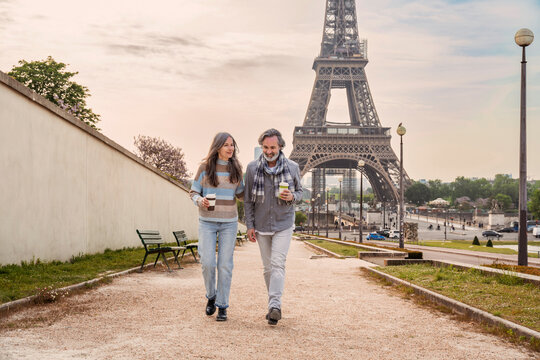 Mature couple with disposable coffee cup walking together in front of Eiffel tower, Paris, France