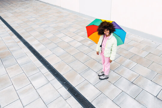 Girl with multi colored umbrella standing on footpath
