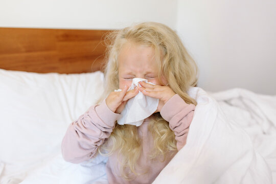 Blond girl blowing nose with tissue paper in bedroom