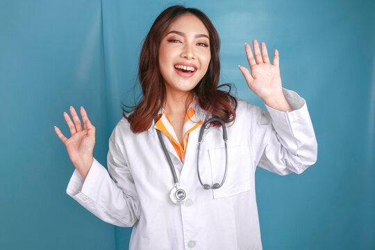 A young Asian female doctor is smiling and giving greeting gesture