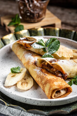 Crepes stuffed with chocolate spread and banana on white plate. Thin pancakes, blini. Delicious breakfast or snack. Food recipe background. Close up