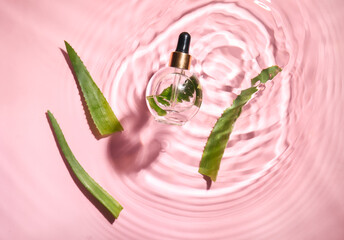 Bottle of natural serum and aloe leaves in water on pink background