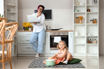 little girl with spoon, toy, cooking pot and her working mother in kitchen