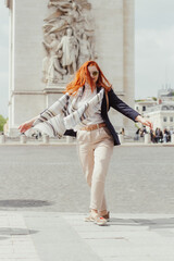 A woman in a navy blazer, cream trousers, wearing a white scarf and spinning in front of the Arc de Triomphe in Paris 