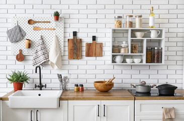 Kitchen counters with utensils and shelf unit on white brick wall