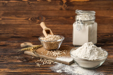 Bowls with flour and wheat on wooden background