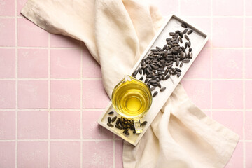Board with jug of oil, sunflower seeds and napkin on pink tile background