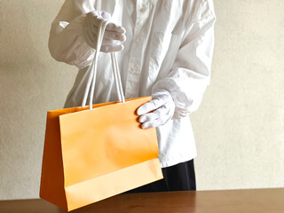 オレンジ色の紙袋を差し出す白手袋をした女性